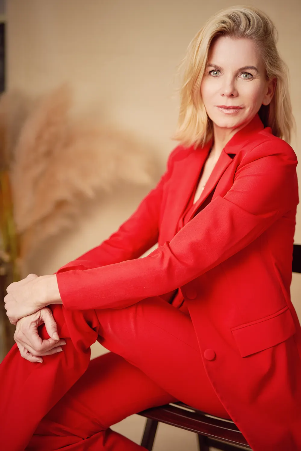 Confident executive portrait of a businesswoman in a red suit, seated in the studio.