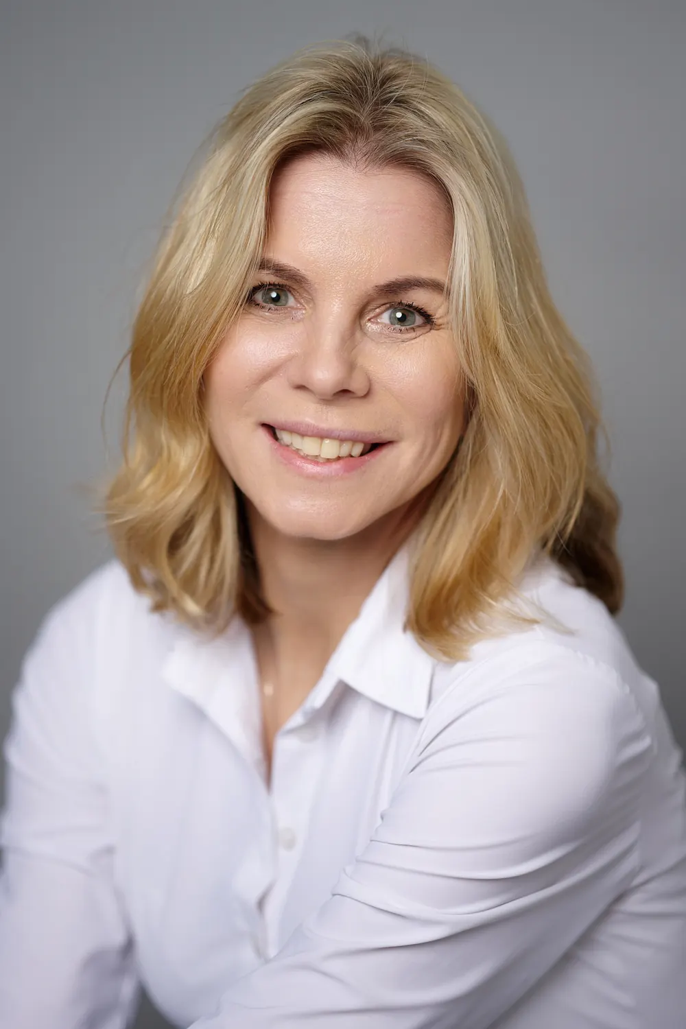 Natürliches LinkedIn Foto einer Frau in weißer Bluse vor grauem Hintergrund.