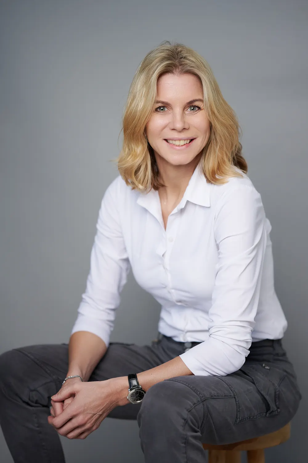 Seated staff portrait of a woman in a white blouse and jeans against neutral grey.